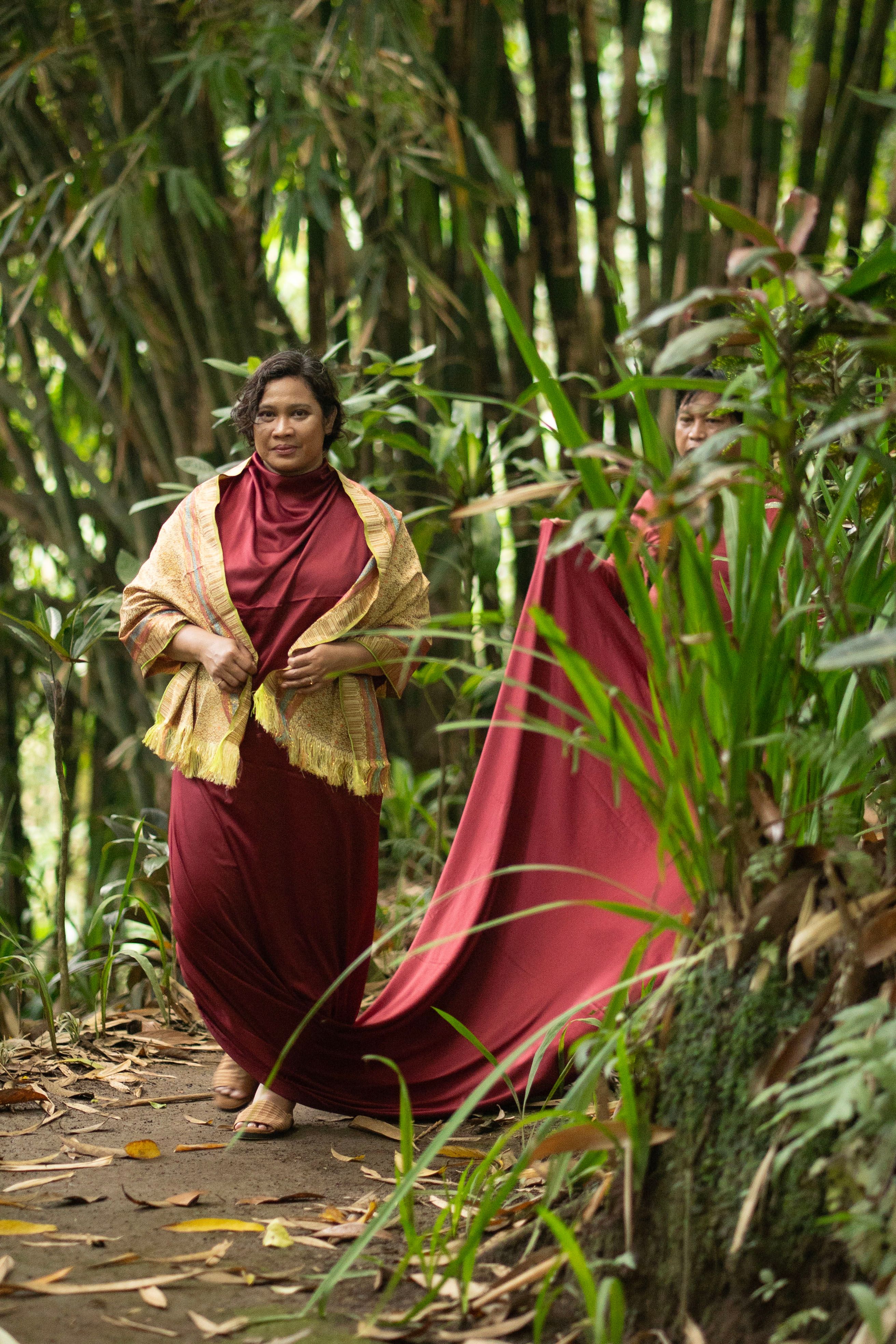 Two women in red traditional attire walking through vibrant jungle path.