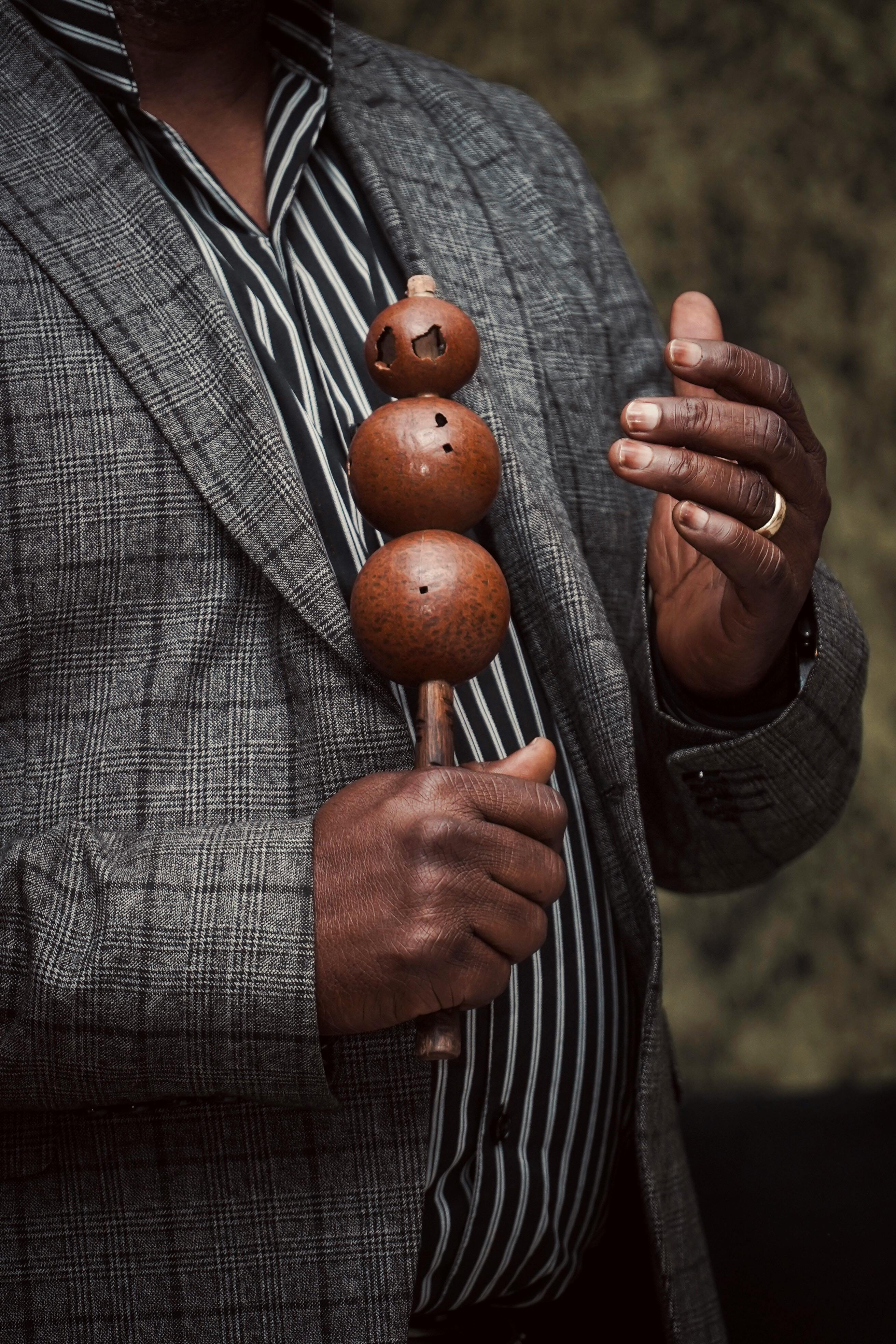 Безкоштовне Крупний план чоловіка, одягненого в смугасту сорочку та блейзер, який тримає шейкер із традиційним африканським дизайном. стокове фото