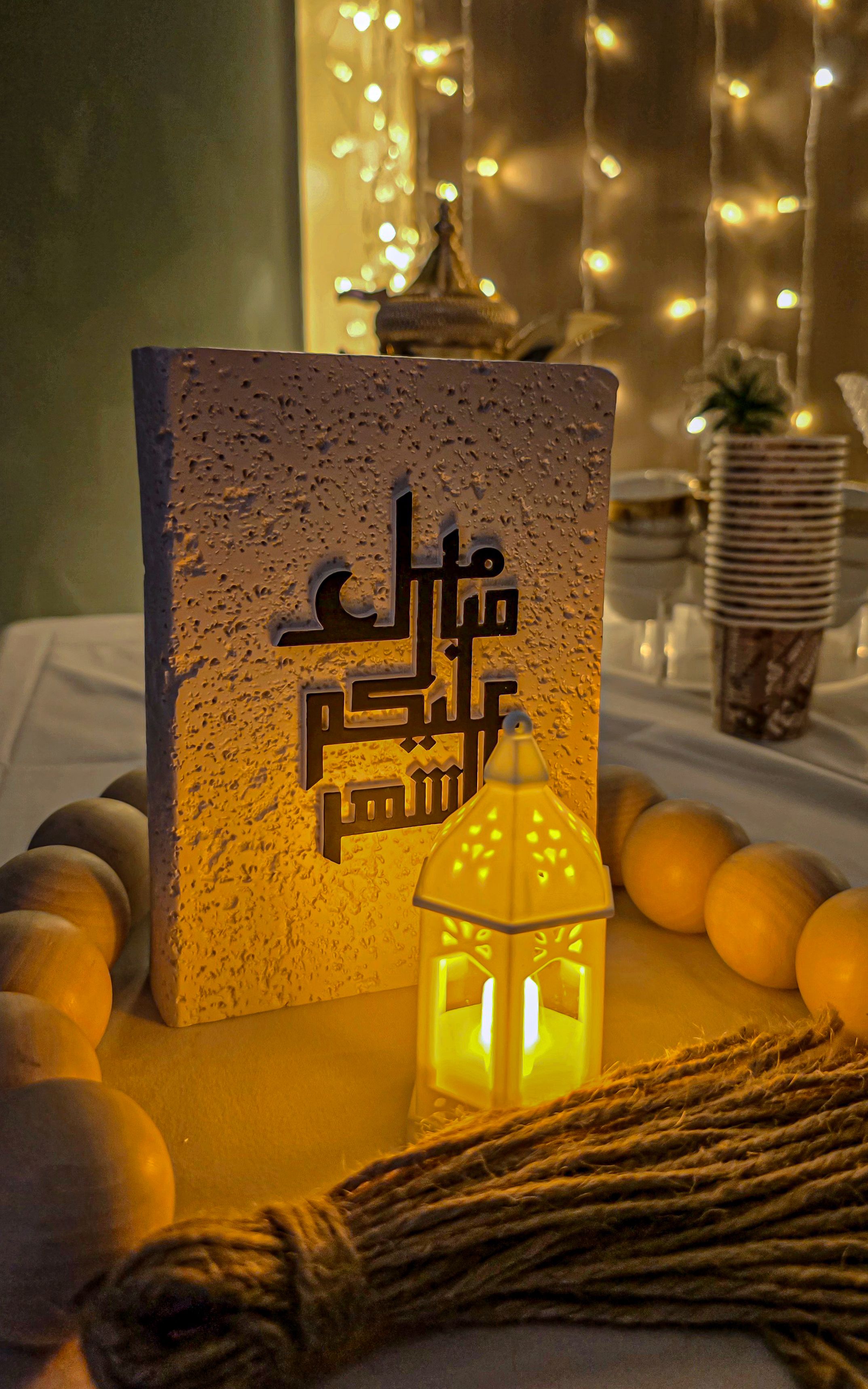Warmly lit scene featuring Arabic calligraphy and a glowing lantern, capturing a festive mood.
