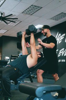 Personal trainer helps client with dumbbell press in Scottsdale gym.