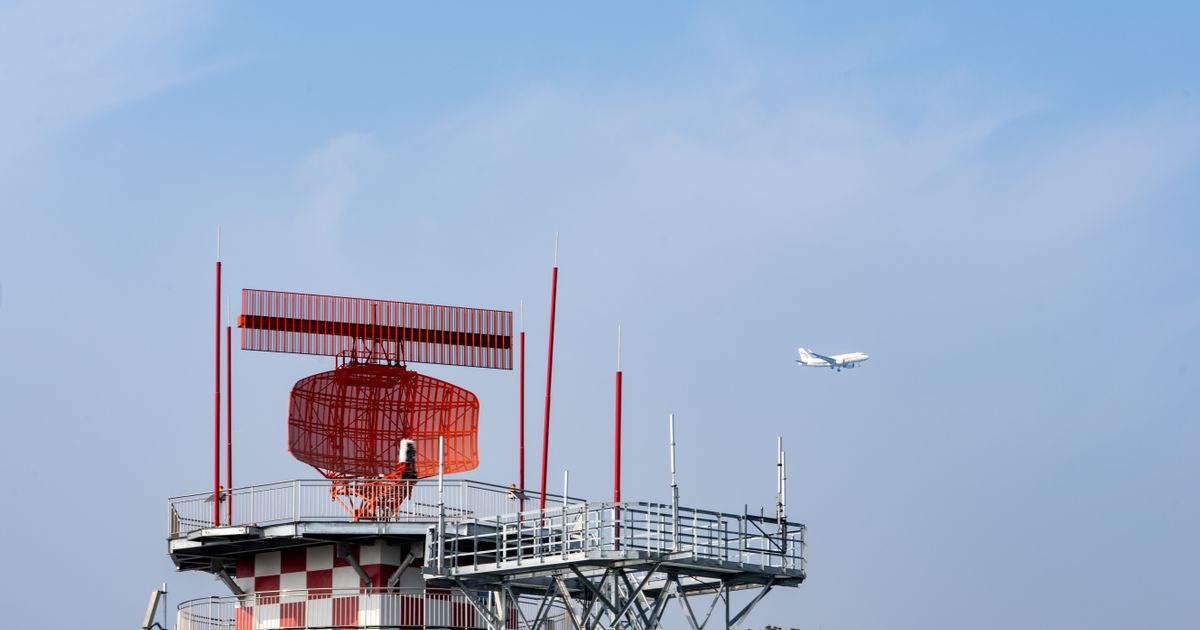 Torre de radar de aeroporto com avião cruzando o céu azul
