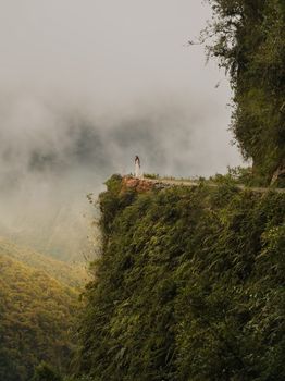 A person stands on the edge of lush mountains on Yungas Road in Coroico, Bolivia.