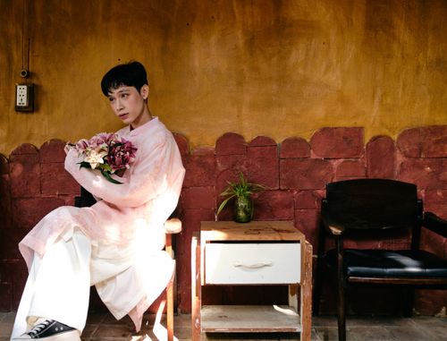 Free Young man in traditional pink Ao Dai holding flowers indoors with cultural decor. Stock Photo