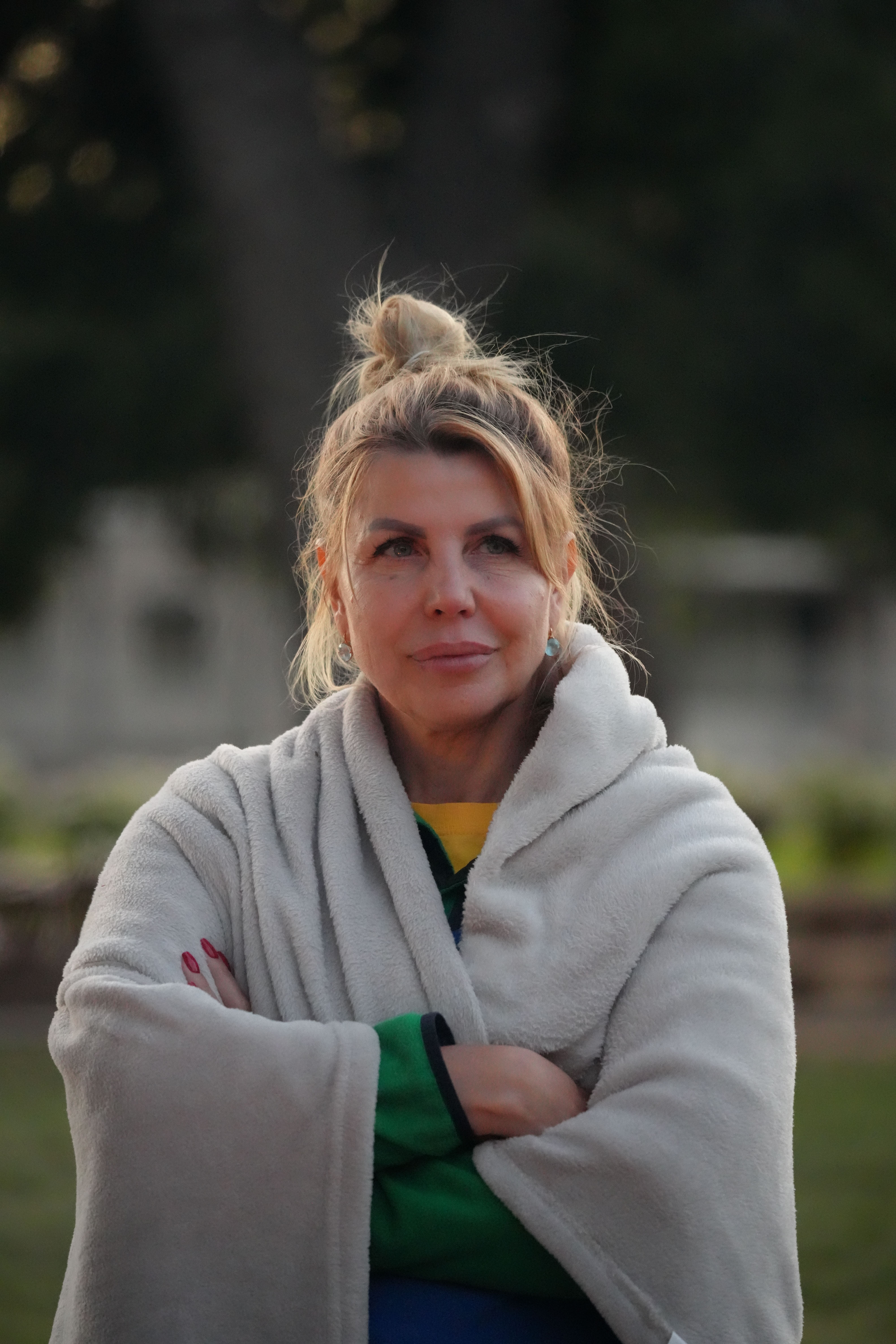 Adult woman stands outdoors wrapped in a cozy blanket.