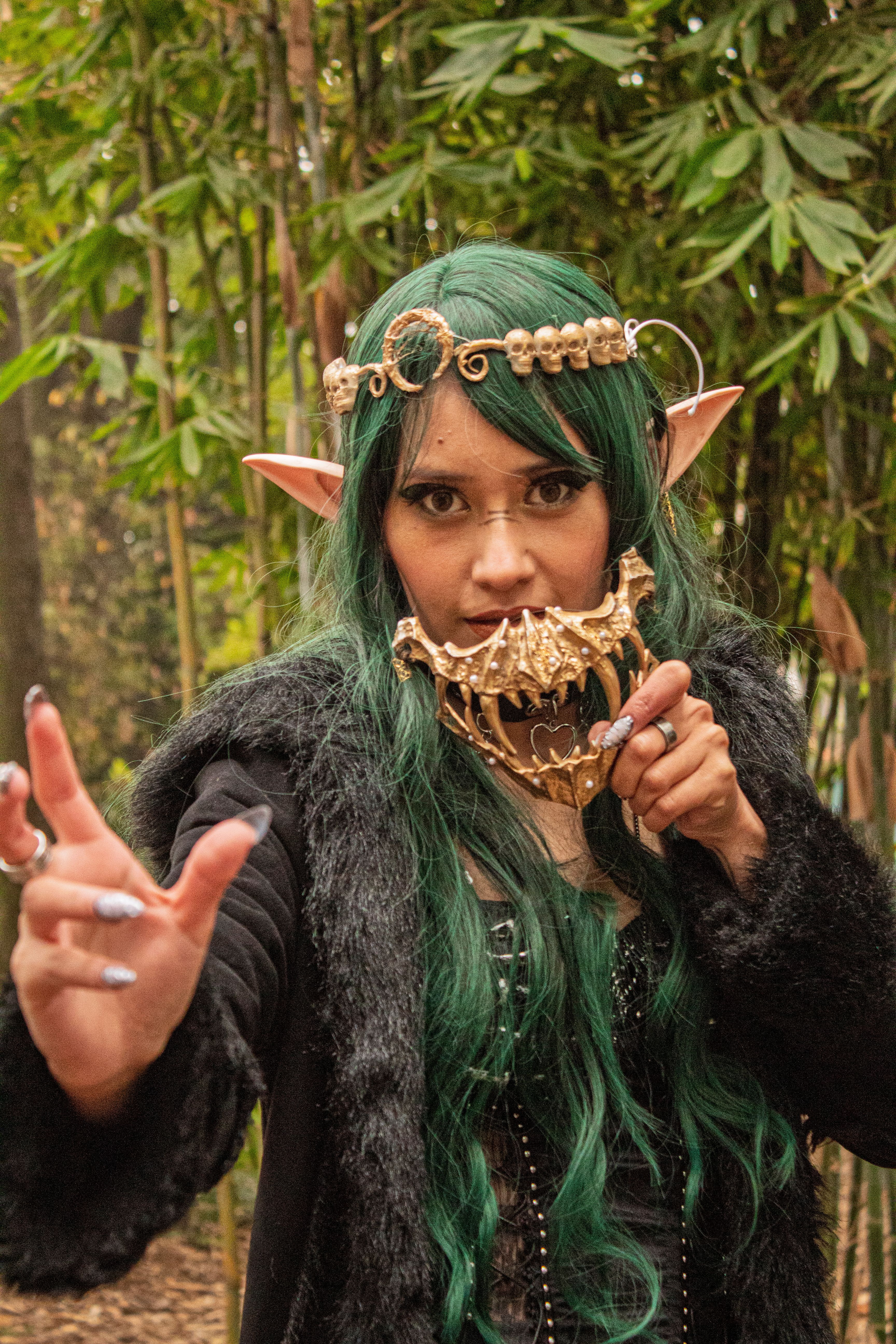 Mystical elf character with intricate headpiece and ornate mask in lush forest setting.