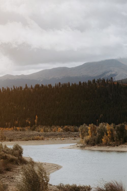 Free Tranquil autumn scene with a winding river and forested mountains under dramatic clouds. Stock Photo