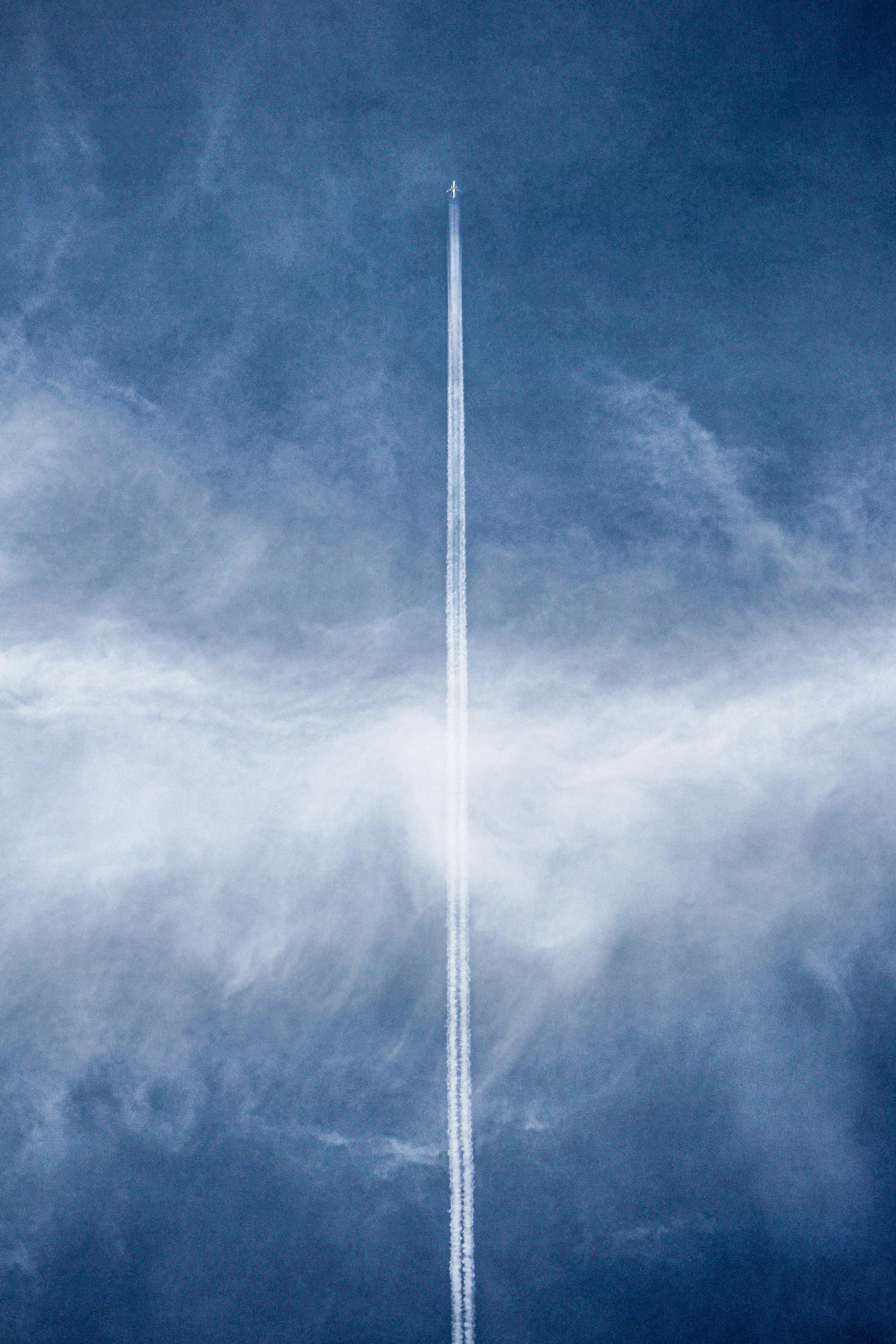 grátis Um avião voando em alta altitude deixa um longo rastro de condensação em um céu azul claro, formando um espetáculo visual deslumbrante. Foto profissional