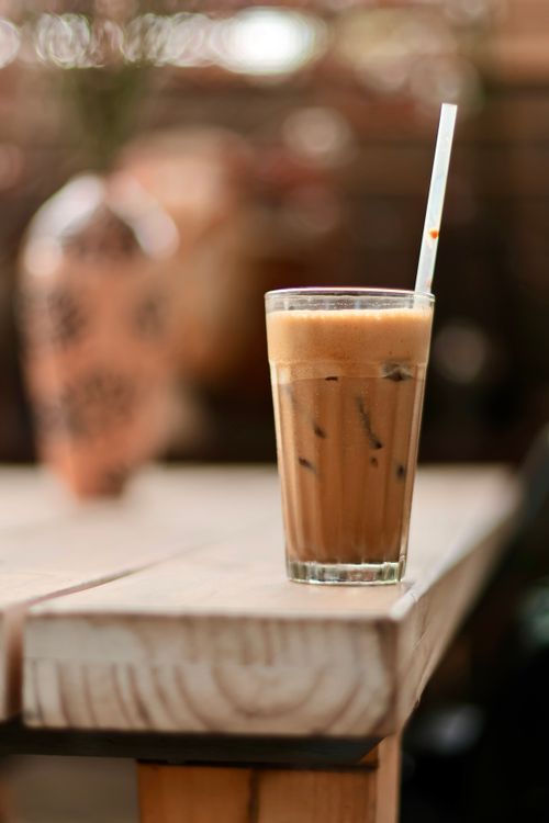 Free A glass of iced coffee with a straw on a wooden table, perfect for a casual cafe setting. Stock Photo