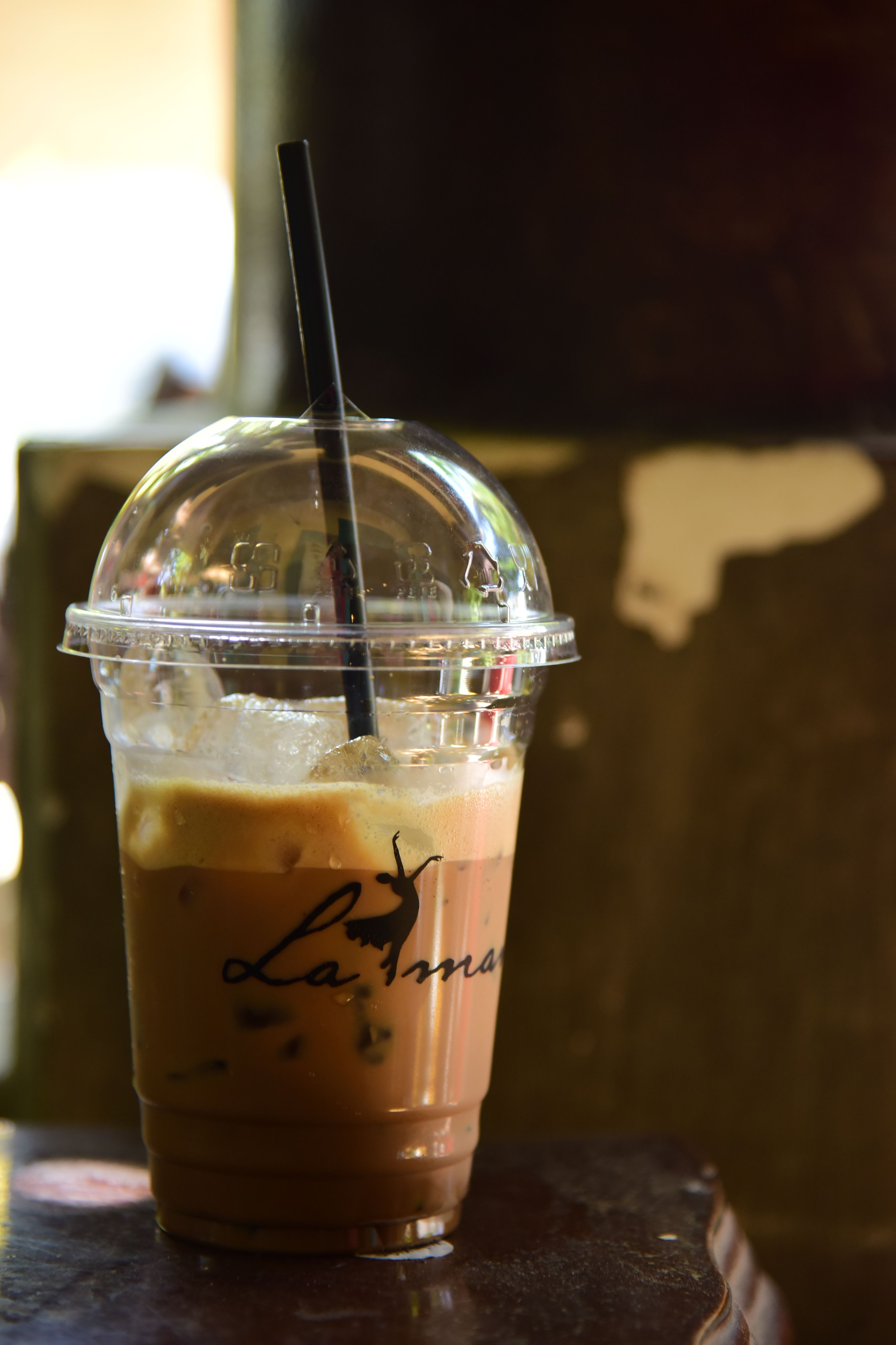 Tall plastic cup filled with iced coffee and a straw on a rustic background.