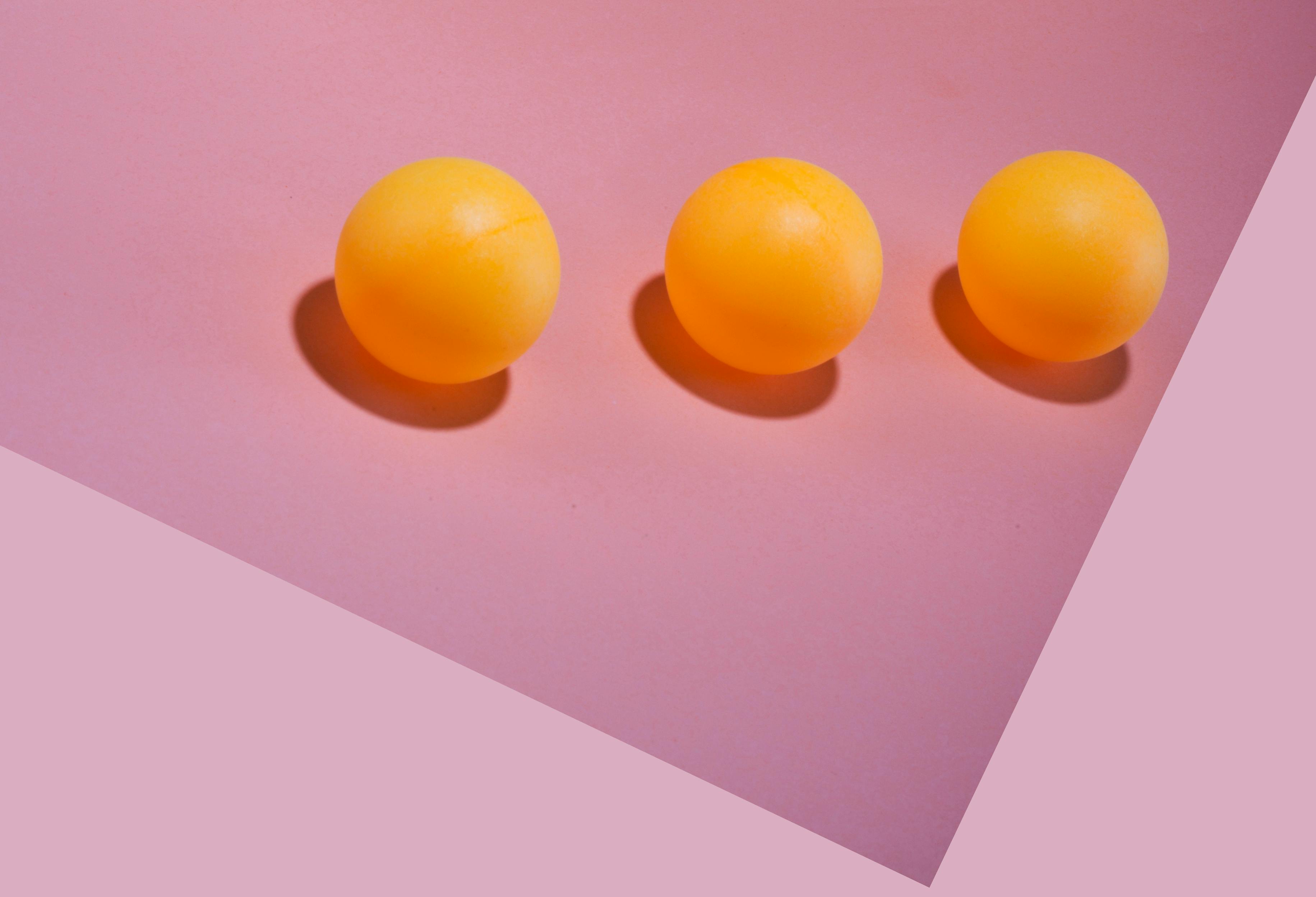De franc Tres pilotes de ping-pong grogues disposades sobre un fons rosa amb ombres geomètriques. Foto d'estoc