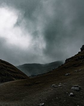 Slopes of wet hilly surface of terrain covered with stones and raindrops traces among clouds in overcast weather in daylight