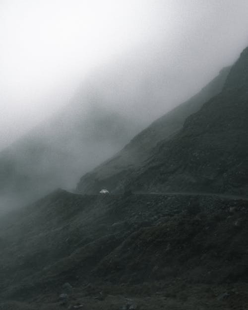 Lonely car driving on narrow road in mountainous valley against gray cloudy sky on foggy day