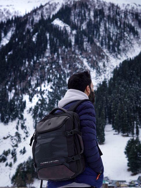 Man standing with a backpack in a snowy mountain landscape, embracing winter adventure with scenic views. - Accessorizing Travel Outfits with Handbags