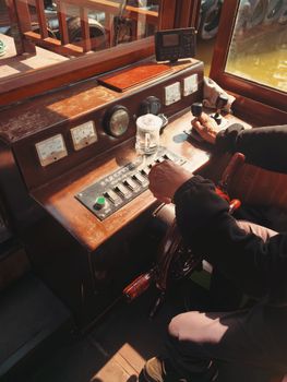 Close-up of a vintage boat cockpit with helm and control panel, highlighting navigation details.