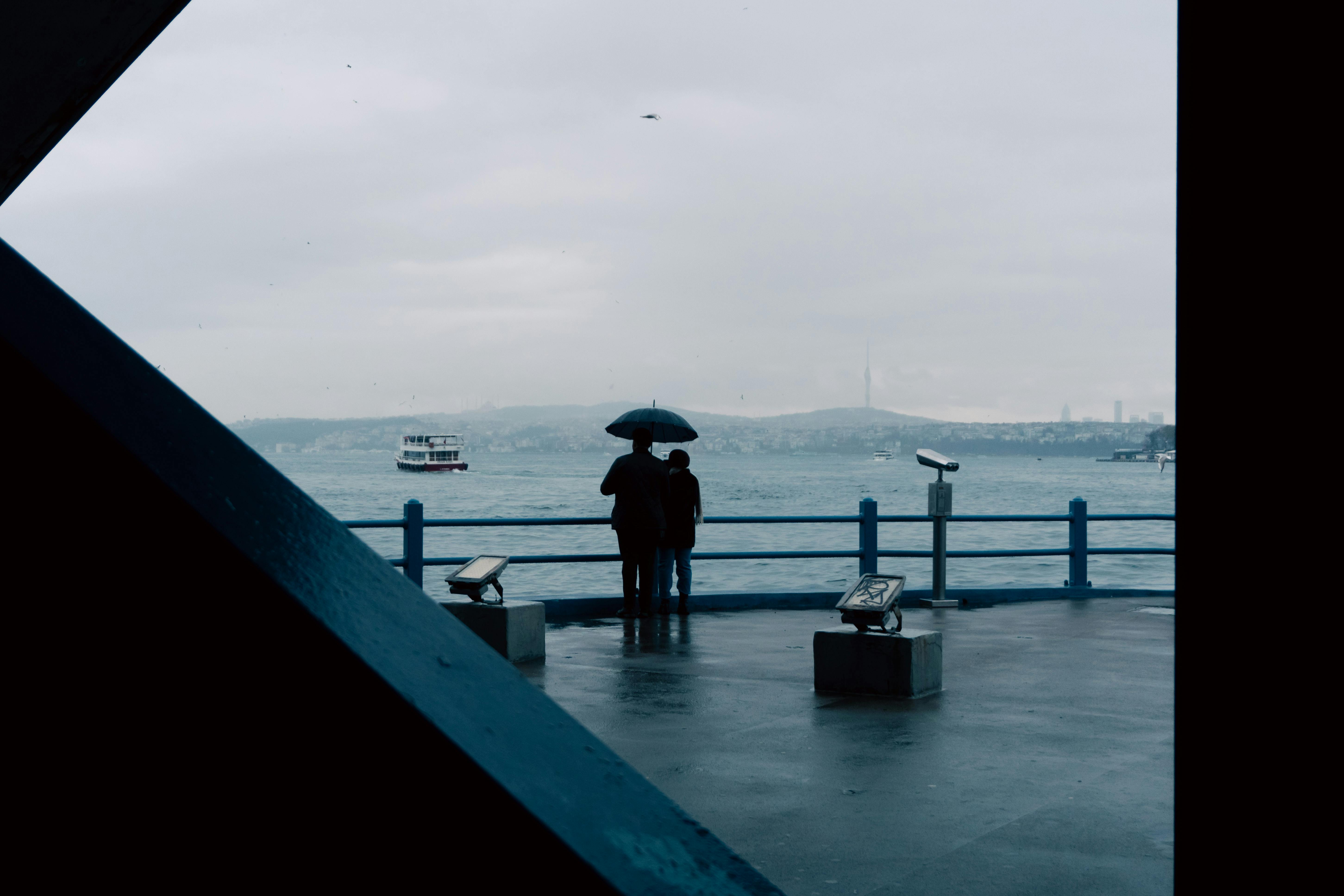 Gratis Una coppia con un ombrello vicino al ponte di Galata a Istanbul in una giornata piovosa, con vista sul Bosforo. Foto a disposizione