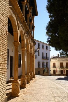 Sunlit stone columns in Spanish plaza with historic buildings.
