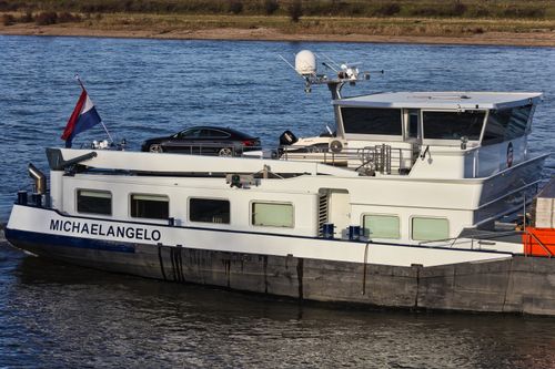 Free Cargo ship named Michaelangelo transporting a car on a calm inland river. Stock Photo