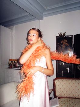 Woman dressed glamorously in room with stylish decor and orange boa.