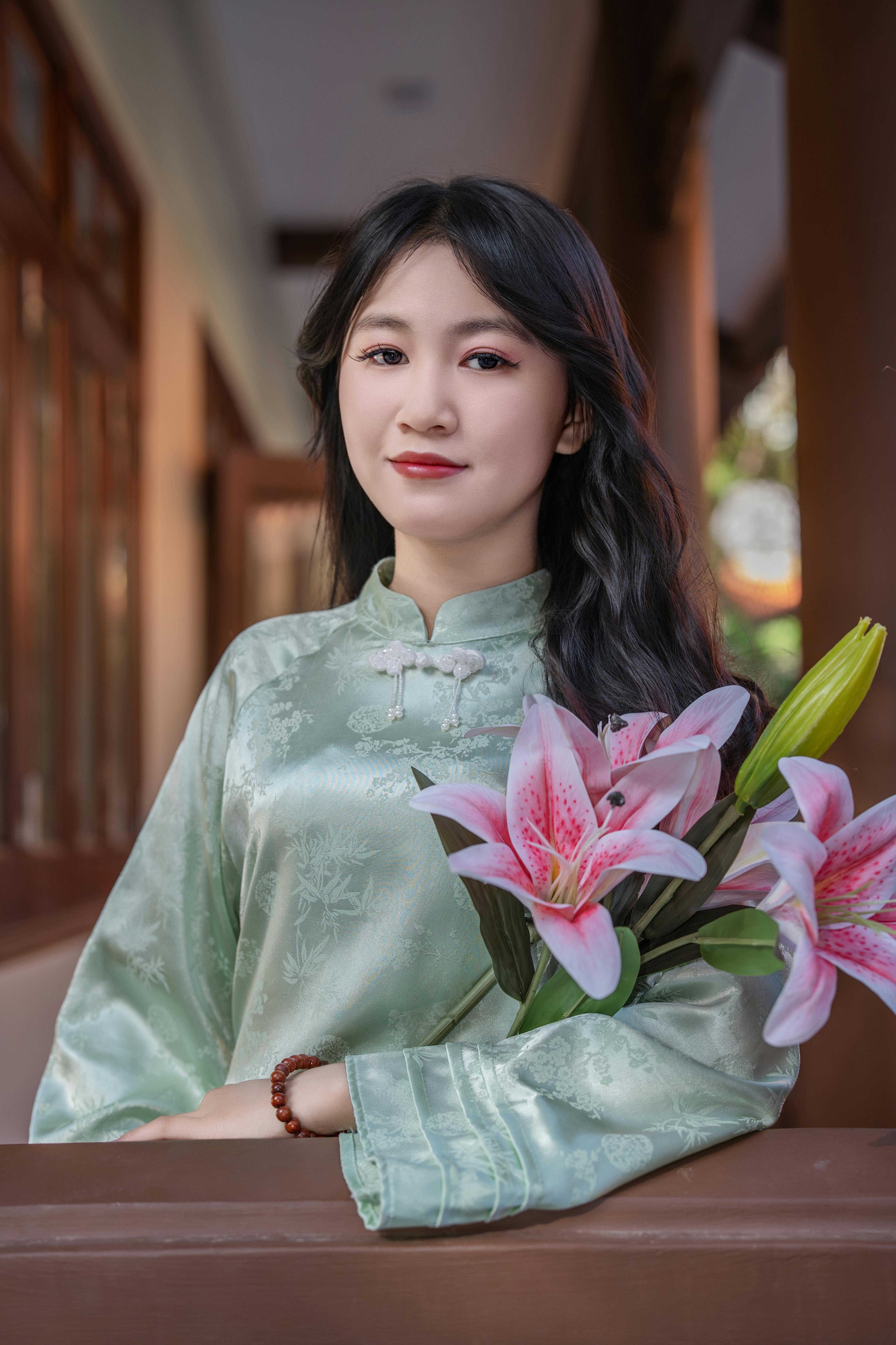 Beautiful woman in traditional attire holding pink lilies, indoors.