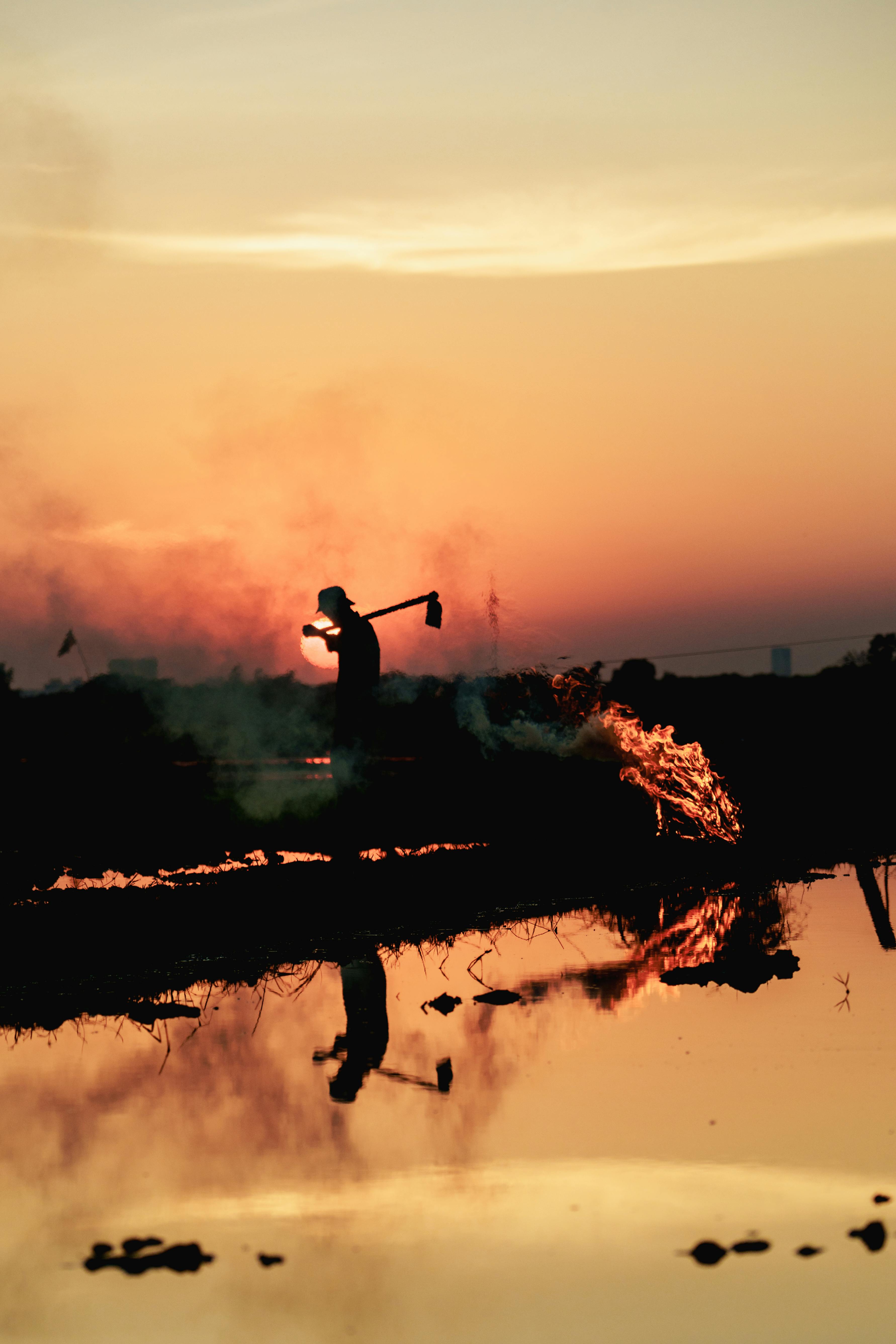 Miễn phí Hình ảnh một người nông dân đơn độc hiện lên trên nền hoàng hôn rực rỡ ở Campuchia, phản chiếu trong cánh đồng ngập nước. Ảnh lưu trữ