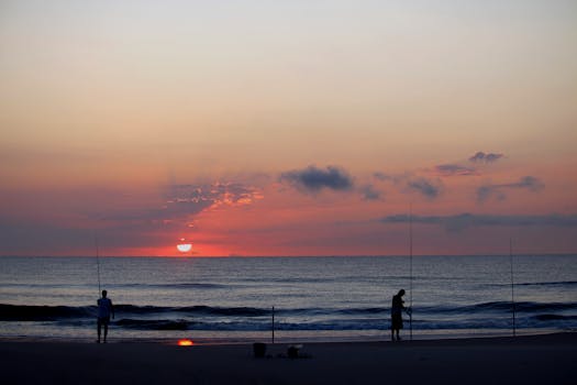 Silhouetted fishermen on Guaratuba Beach at sunrise, capturing the tranquil beauty of the ocean and colorful sky.
