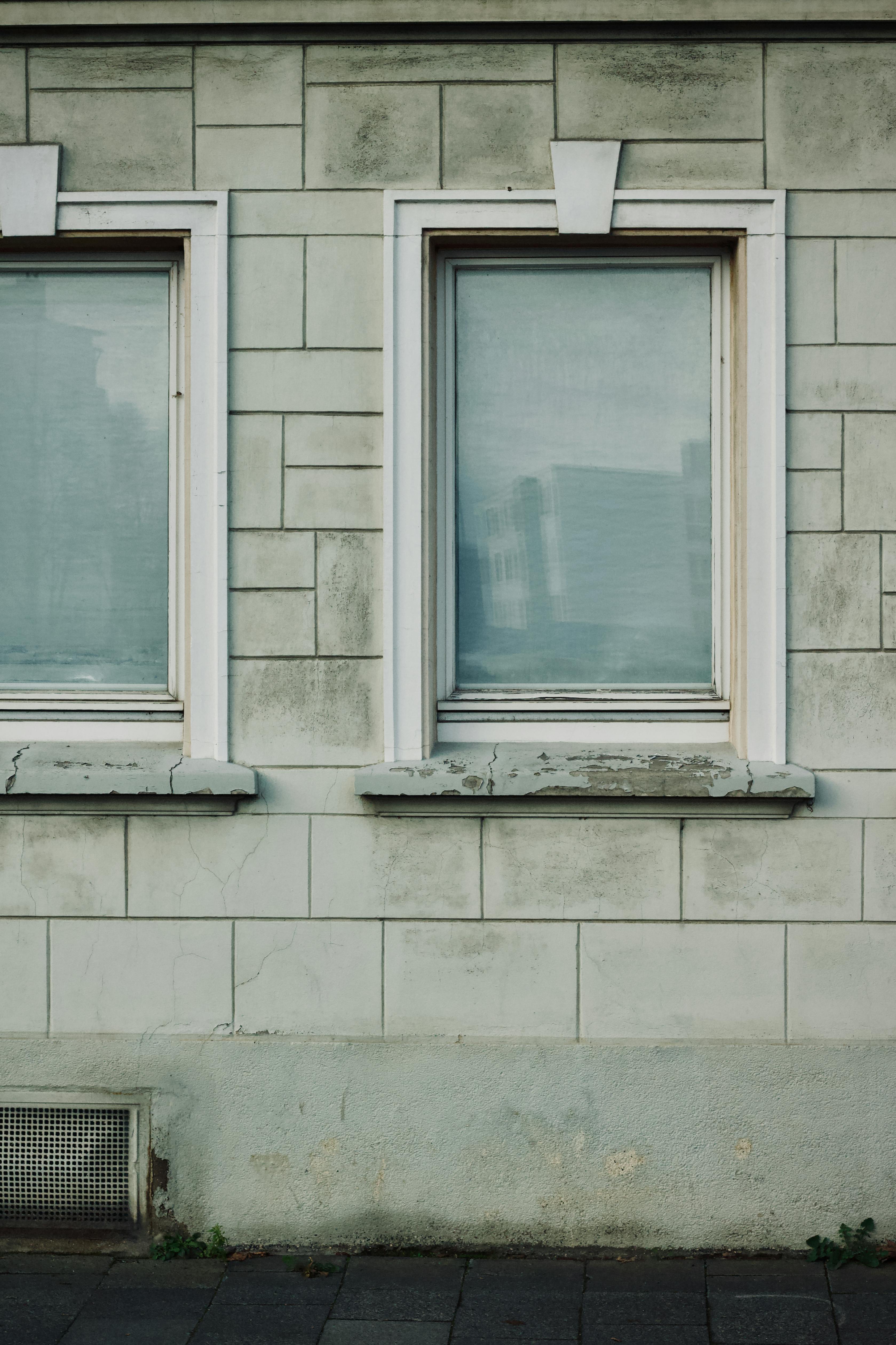 grátis Detalhe da fachada de um edifício com duas janelas fechadas em uma parede texturizada. Foto profissional