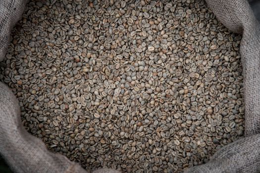 Close-up of unroasted green coffee beans in a burlap sack, showcasing rustic texture and natural color.