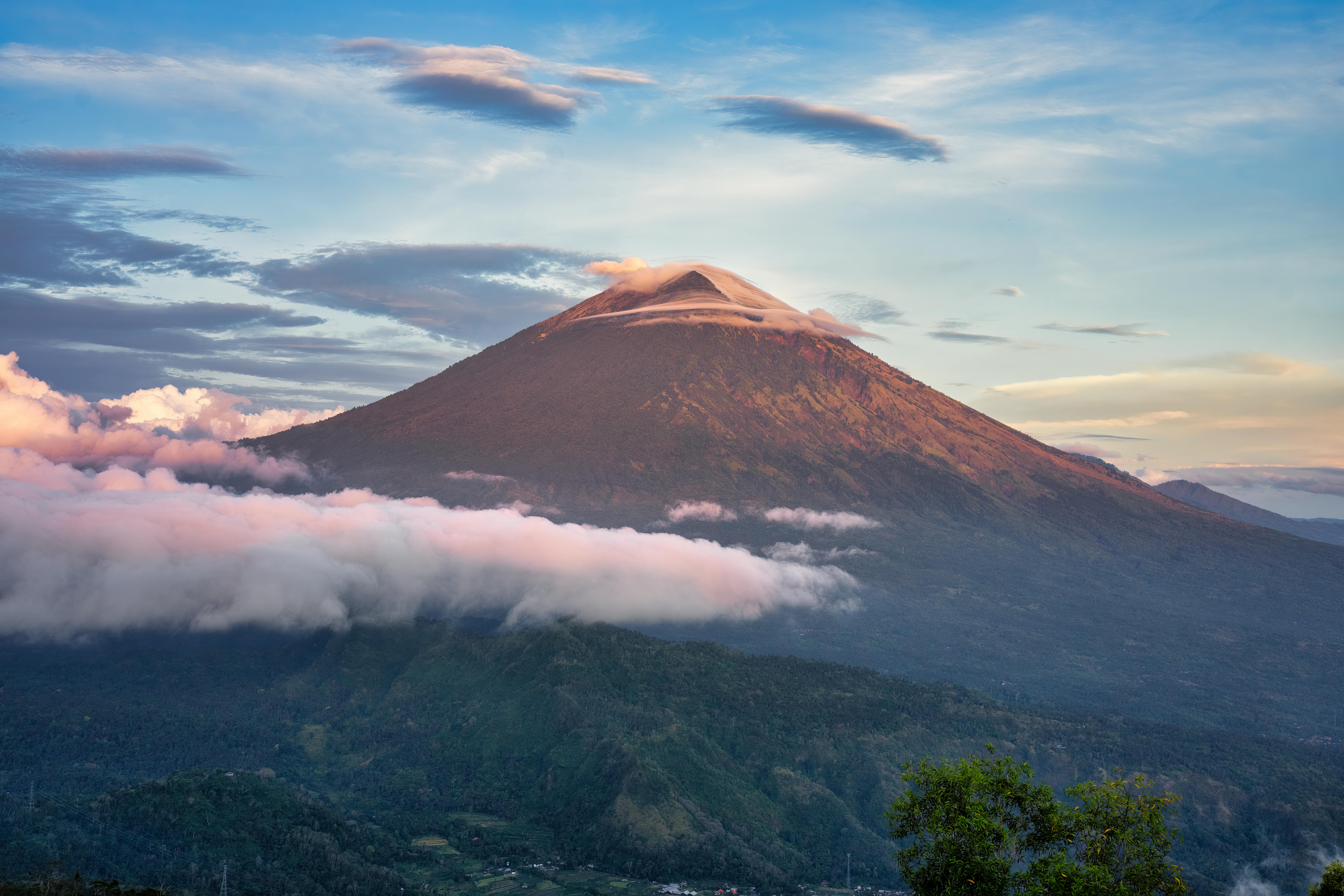 Hikers watching sunrise from the summit of Mount Batur volcano with Mount Agung in the distance, Bali