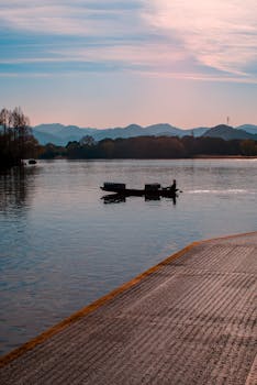 Tranquil scene of a boat on a lake at sunset with distant mountains.