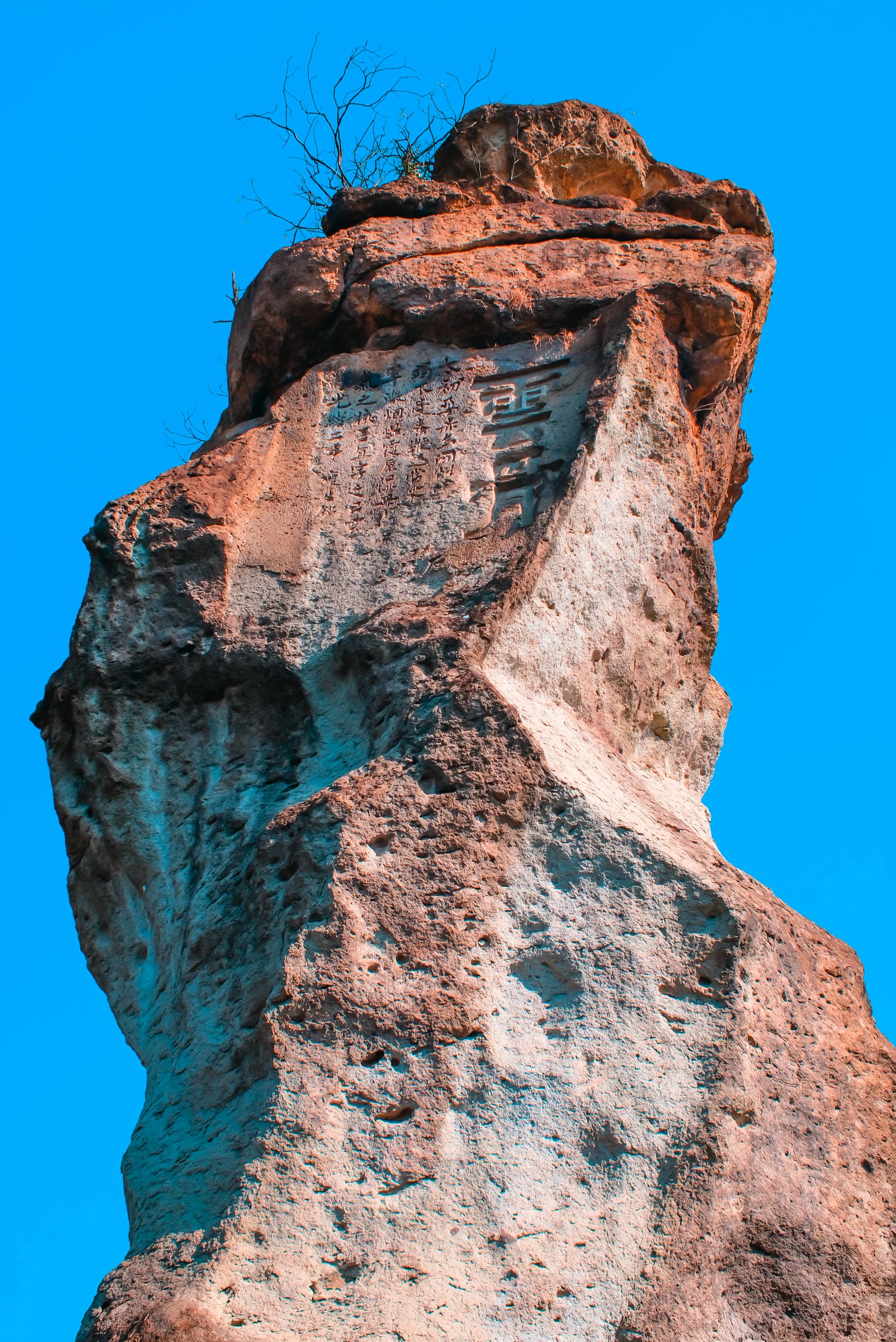 Free Dramatic rock formation reaches skyward, carved with mysterious inscriptions against a vibrant blue sky. Stock Photo