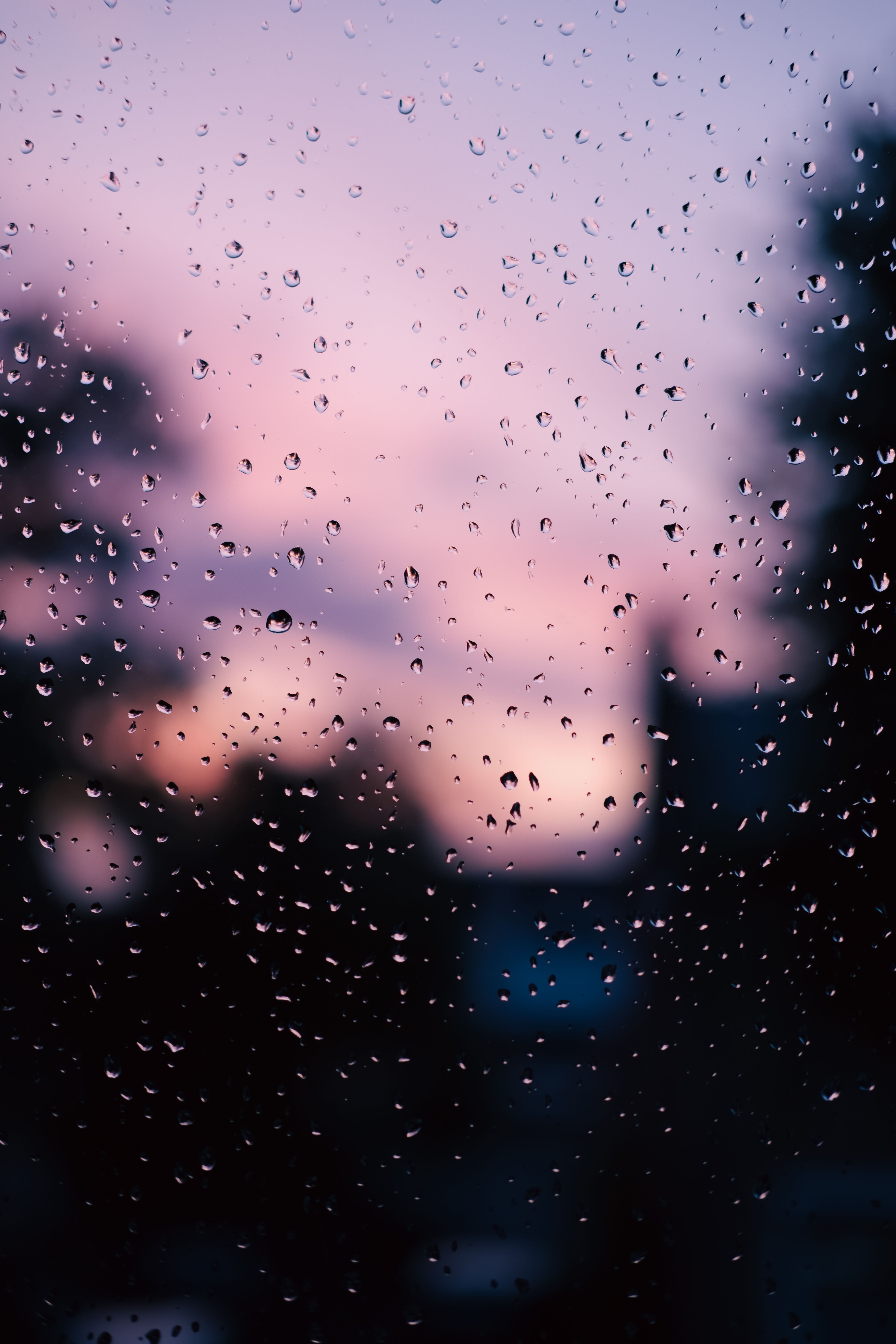 Rain droplets on glass with a colorful sunset backdrop. Tranquil and reflective mood.