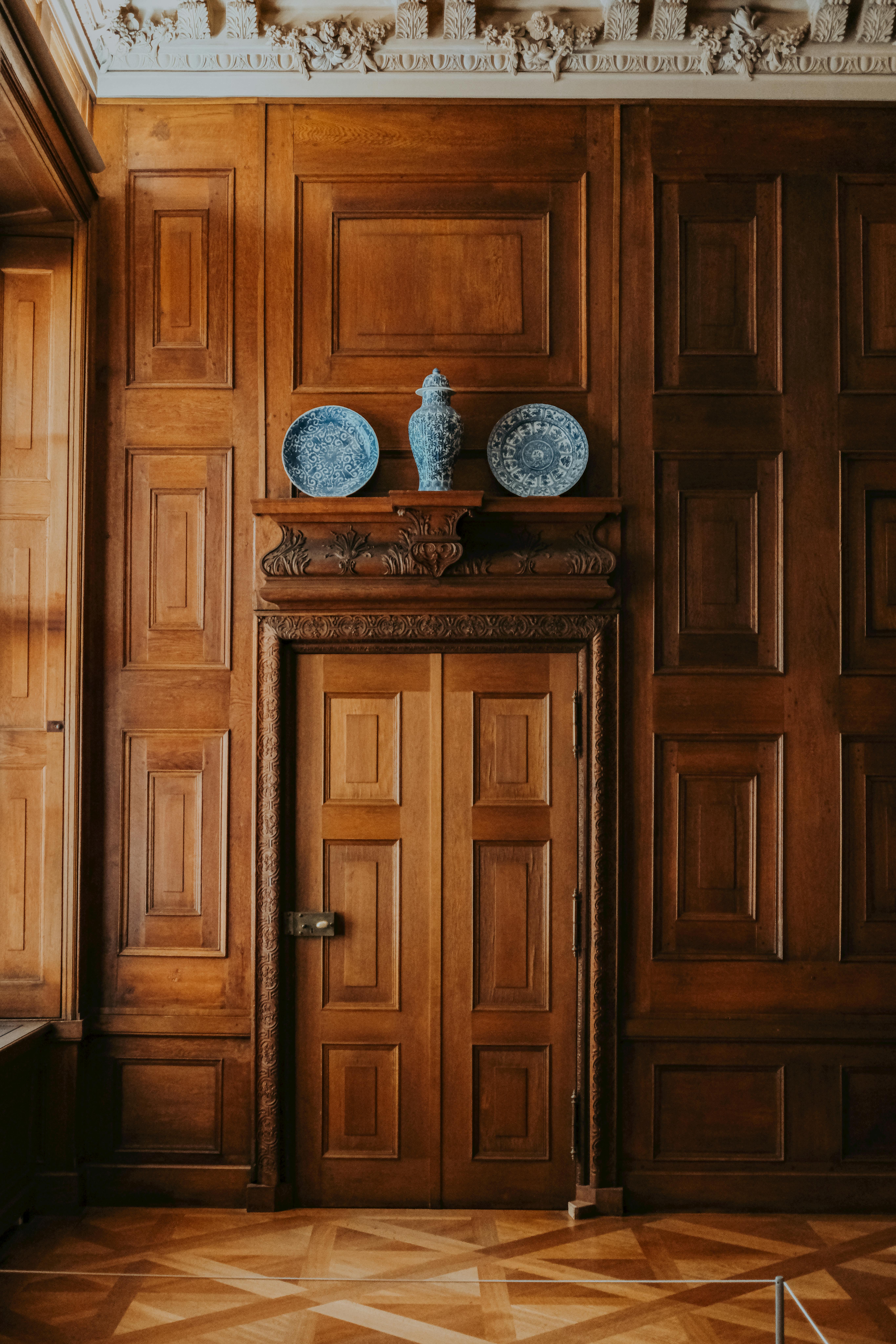 De franc Un espai interior clàssic amb panells de fusta complexos i ceràmica decorativa sobre una porta de fusta. Foto d'estoc