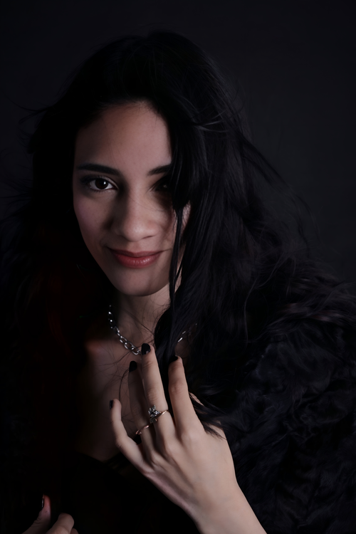 Free A stylish portrait of a smiling woman with dark hair and jewelry against a dark background. Stock Photo