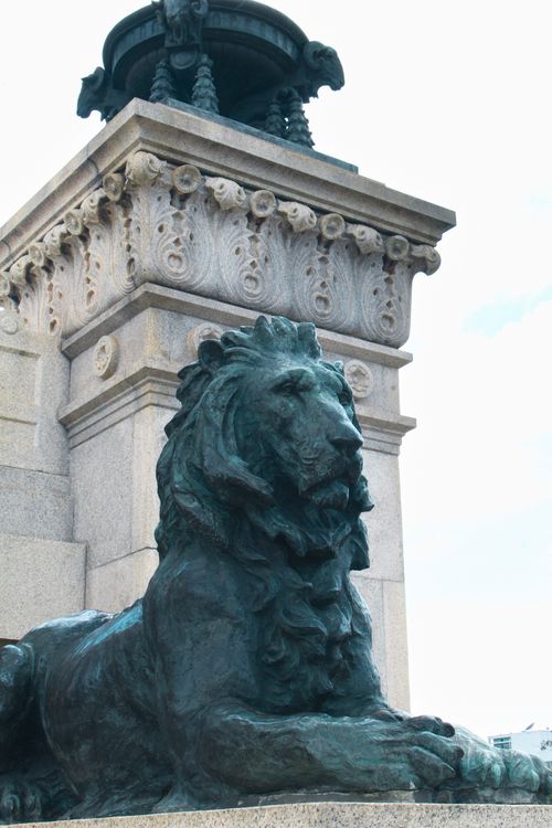 Free A majestic lion statue sits at the base of an ornate monument in daylight. Stock Photo