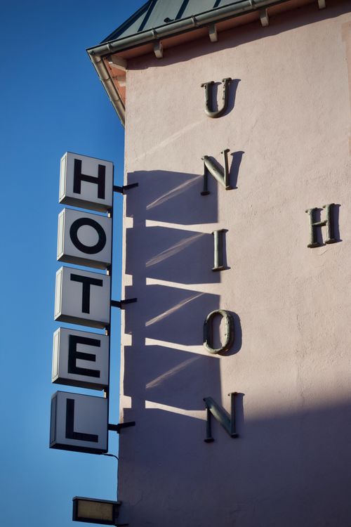 Free Vertical sign for Hotel Union with clear shadows on an exterior wall, sunny day view. Stock Photo