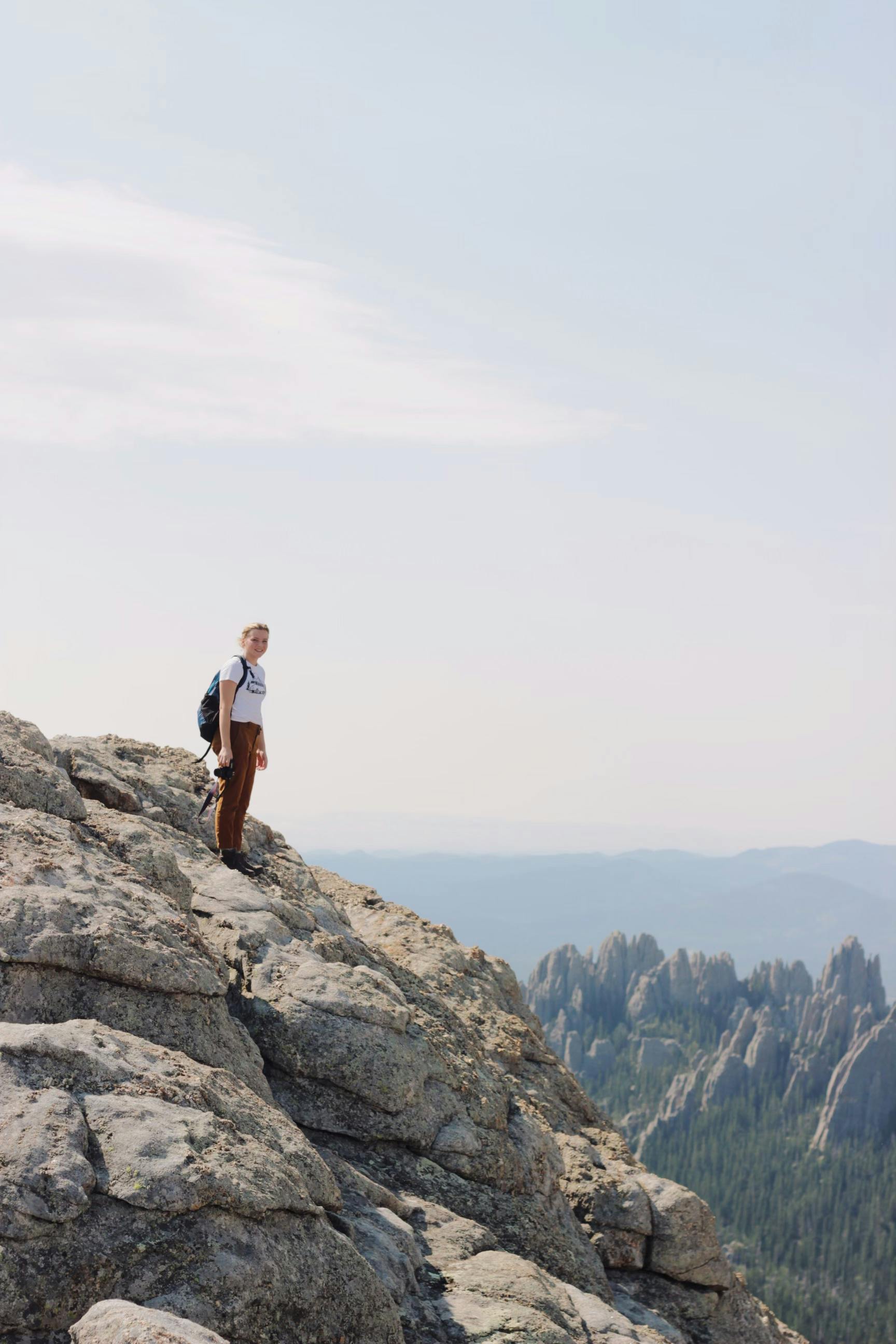 A lone hiker standing on a rocky cliff enjoys a panoramic view of distant mountains.