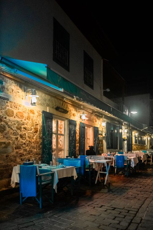 Free Cozy outdoor dining at a charming Mediterranean restaurant with vibrant blue chairs and a rustic stone wall. Stock Photo