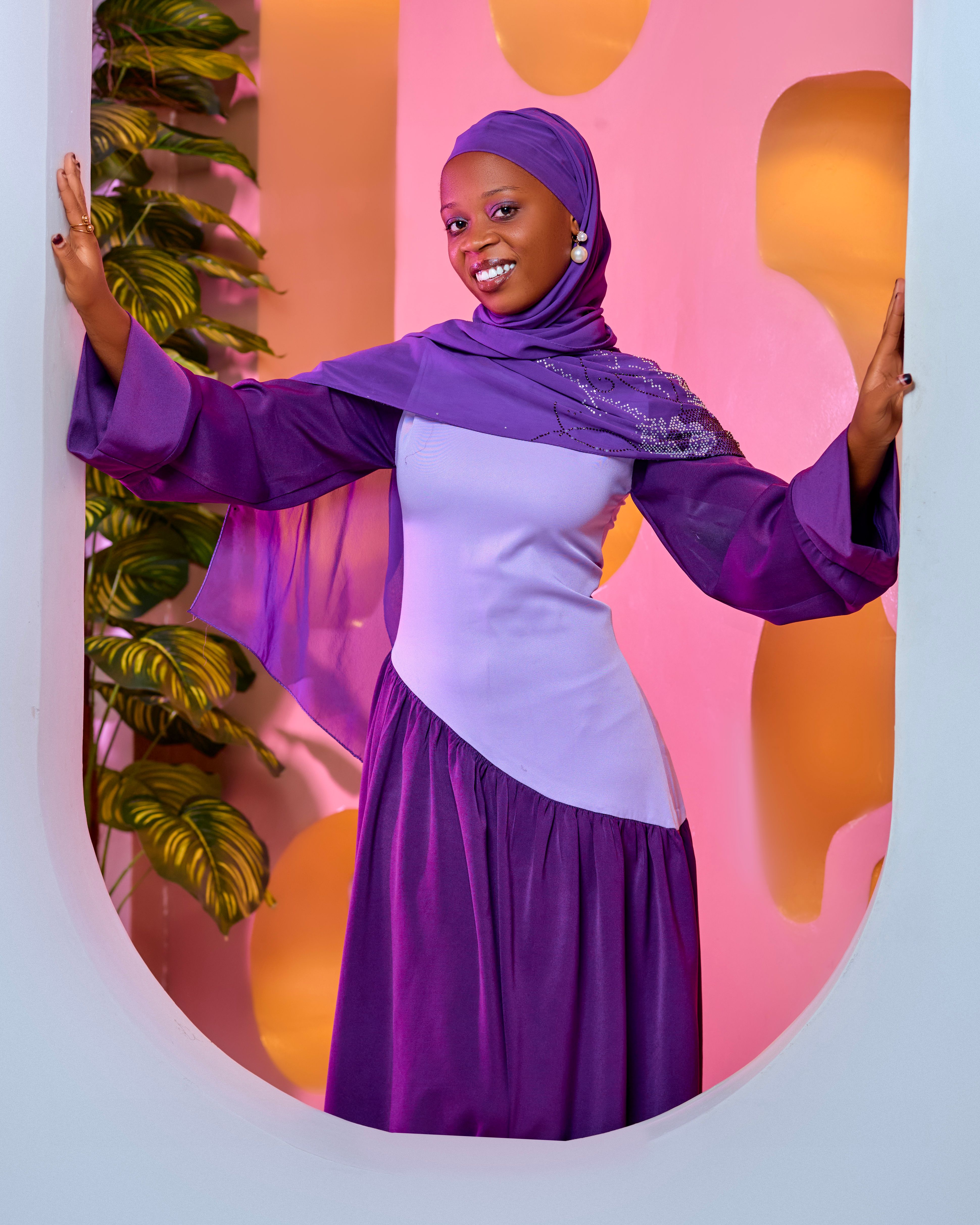 Elegant portrait of a woman in a vibrant purple hijab and dress, smiling indoors.