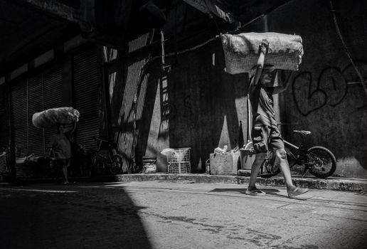 Dynamic black and white street scene of men carrying heavy bundles in an urban alley.