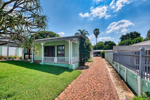 Lovely suburban house with lush garden and long driveway under a clear blue sky.