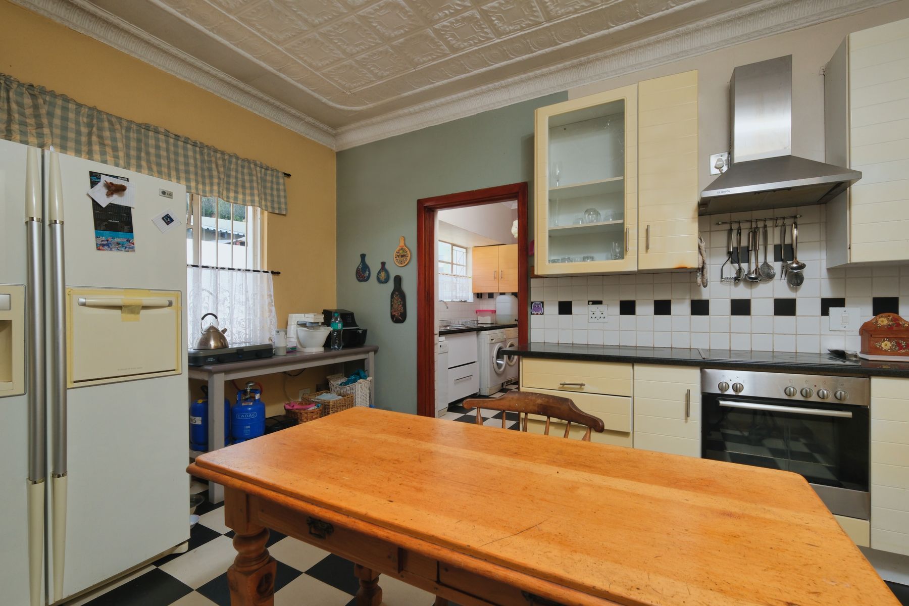Wood kitchen table with cream cabinetry, pale green wall and black-and-white floor