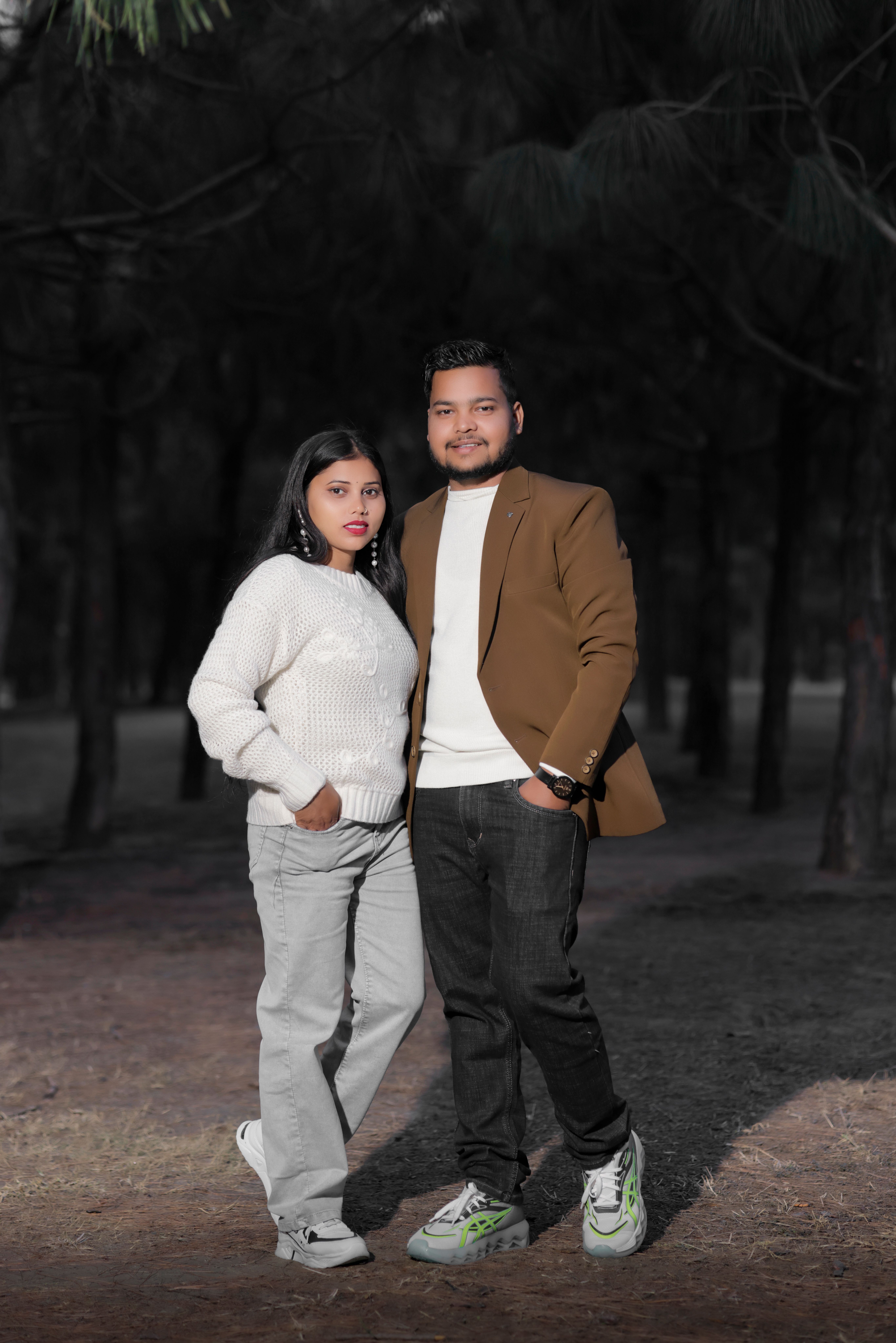 A couple poses together in a forest, enjoying a casual outdoor setting.