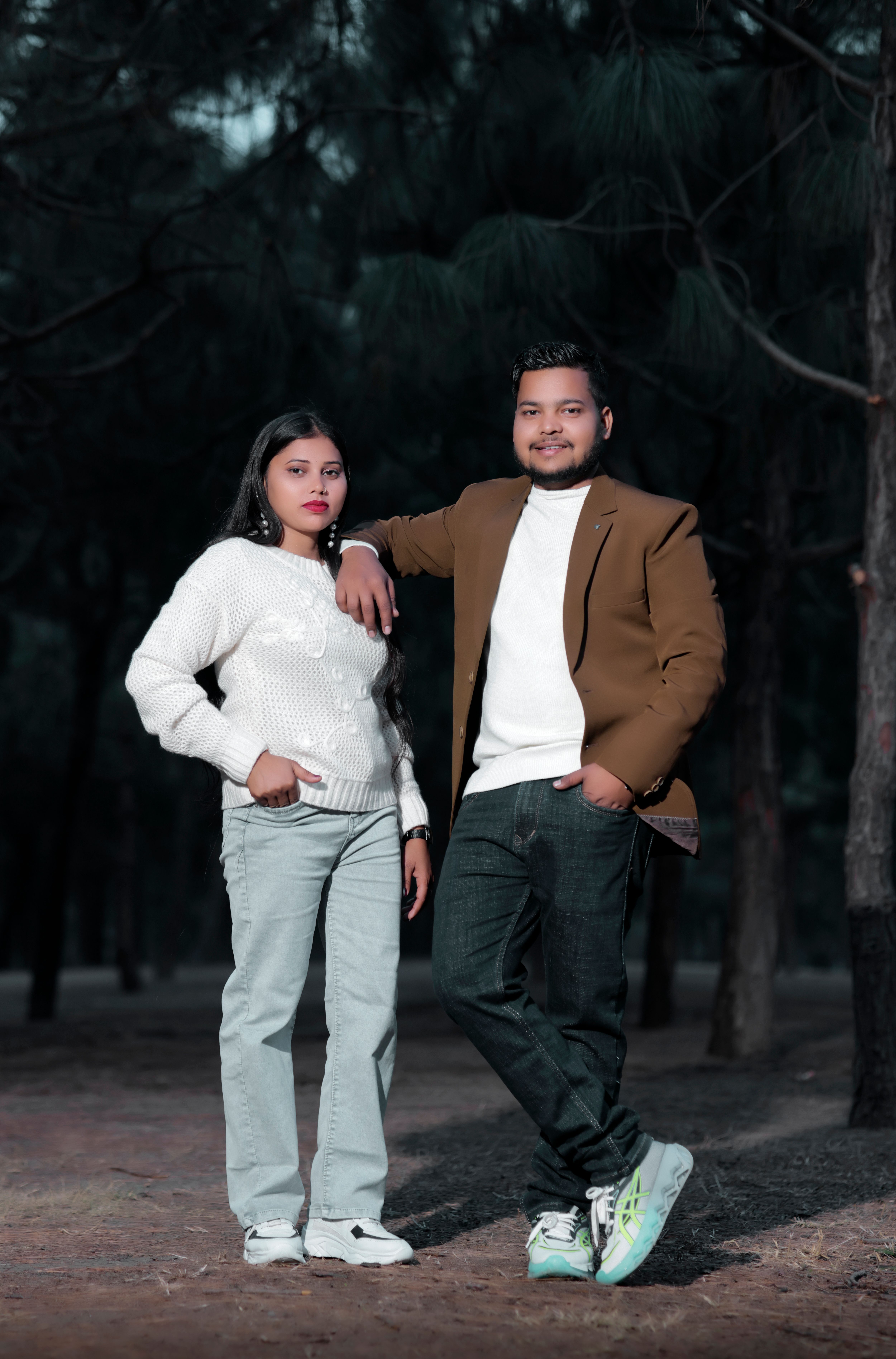 Young couple posing casually in outdoor woodland setting, showcasing fashion and companionship.