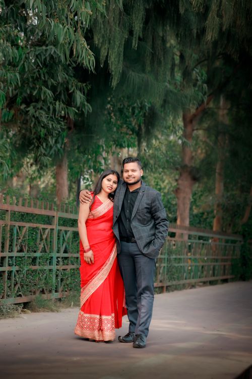 Free A couple in formal attire posing together outdoors with greenery in the background, conveying romance. Stock Photo