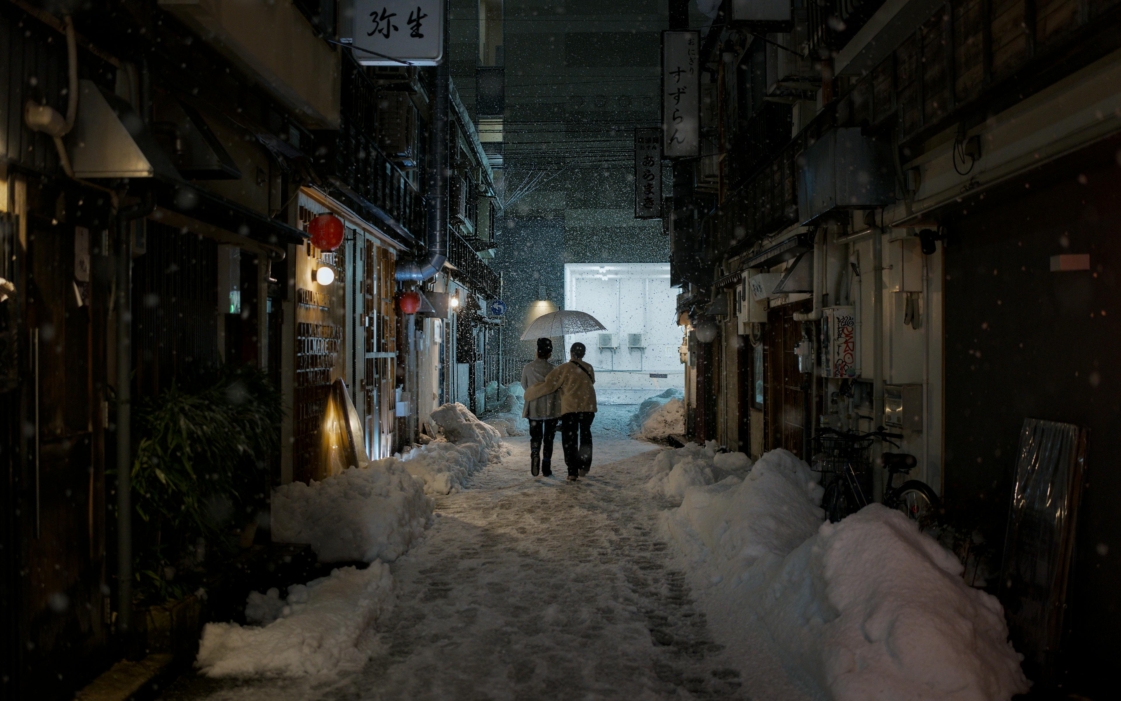 Couple walking under an umbrella in a snow-covered alley in Kanazawa, Japan at night.