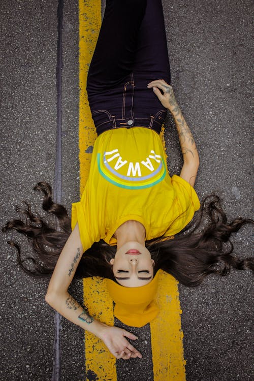 Free Woman in Yellow and Black T-shirt Lying on Grey Concrete Floor Stock Photo