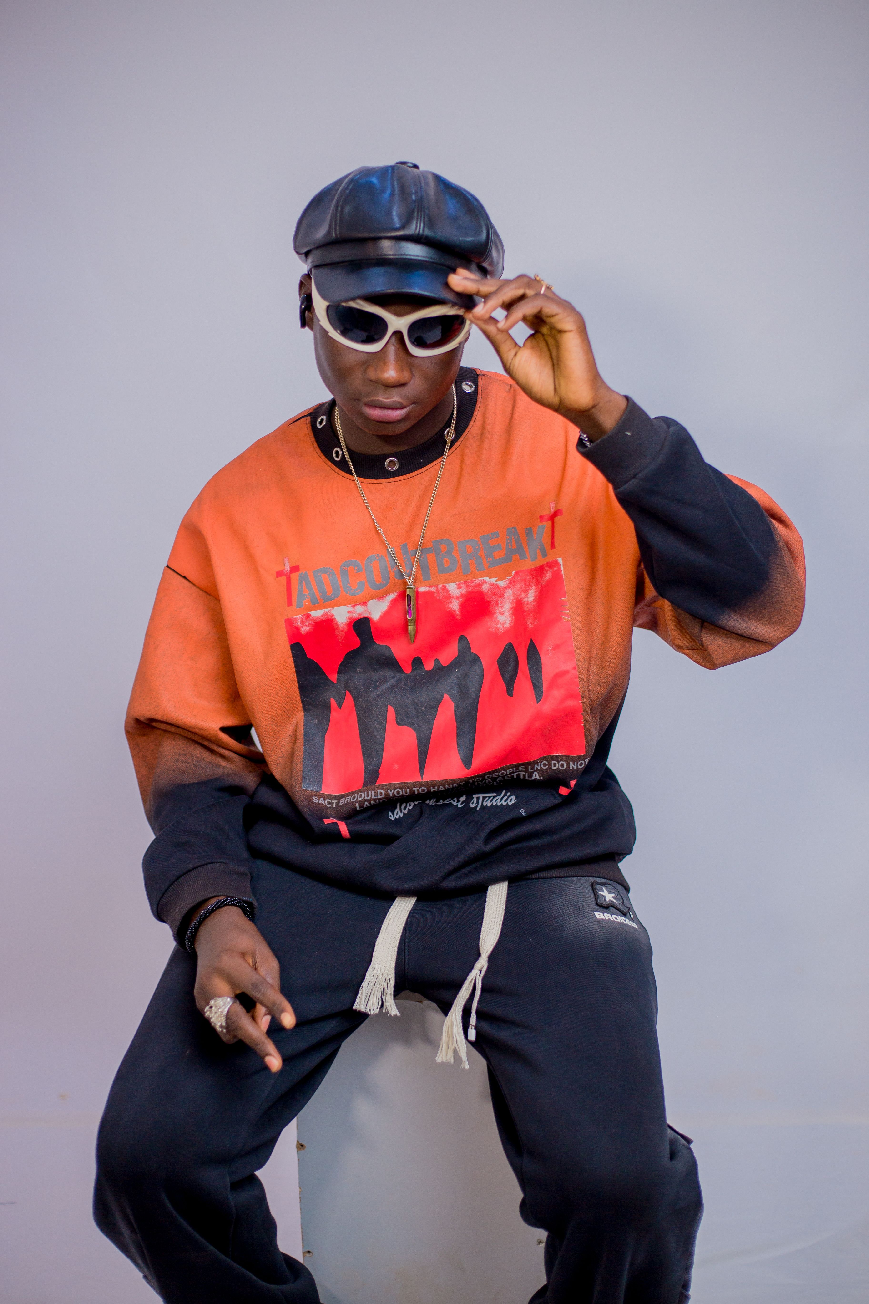 Young man in urban streetwear poses confidently with sunglasses indoors.