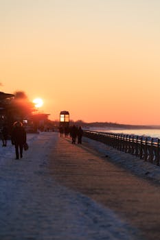 Serene winter sunset scene on Zelenogradsk boardwalk with silhouettes of people walking by the coast.
