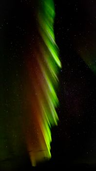Vivid aurora borealis with green and red hues illuminating a clear, star-filled night sky.