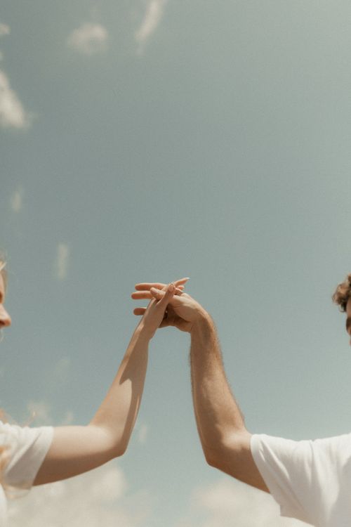 Free Close-up of a couple holding hands against a blue sky, symbolizing unity and love. Stock Photo